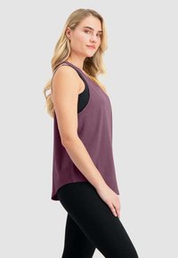 Lila ärmelloses Oberteil mit einem lässigen Schnitt, weicher Textur, abgerundetem Saum und auffälligen Armausschnitten, über einem schwarzen Tanktop getragen.