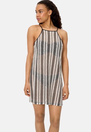 Mujer con cabello rizado que lleva un vestido sin mangas hasta la rodilla con un patrón de encaje a rayas verticales en blanco y negro, posando contra un fondo liso.