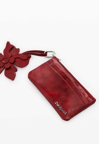 Rotes Lederportemonnaie mit Reißverschluss, versehen mit einem großen floralen Akzent und einem angebundenen Handgelenkriemen. Text "Desigual!" auf der Oberfläche.