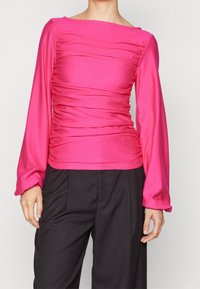 Fuchsia långärmad topp med texturerad rynkning längs framsidan och ärmarna, fyrkantig halsringning, bärs med svarta högmidjade byxor.