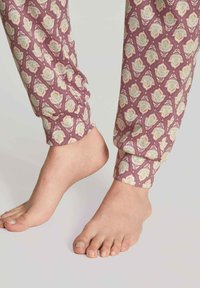 Paarse pyjamabroek met een bloemmotief in groene en perzikaccenten. De boorden zijn elastisch. Blote voet zichtbaar aan de onderkant.