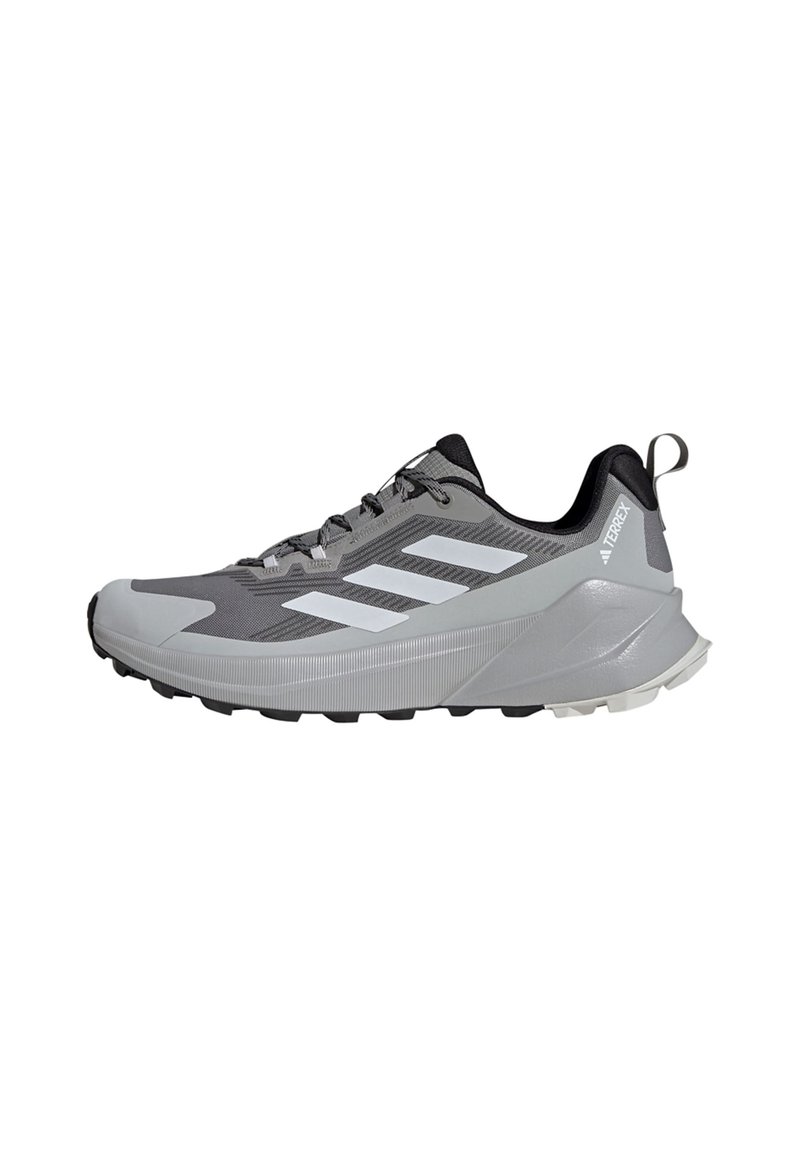 Zapatilla deportiva de color gris claro con una parte superior de malla texturizada, acentos negros, un distintivo logotipo de tres rayas y una suela negra resistente para tracción.