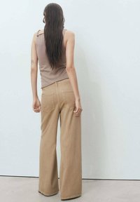 Brown tank top paired with wide-leg beige trousers, featuring a soft texture, regular fit, and back pockets, with a minimalist design.