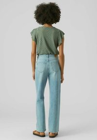 Top verde a maniche corte con motivo a occhiello abbinato a jeans dritti a vita alta blu chiaro e sandali neri flat.