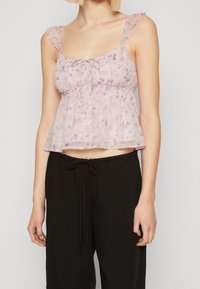 Genomskinlig lavendelfärgad blommig crop top med volangdetaljer på axelbanden, knytning vid halsringningen och insvängd midja. Matchas med lösa svarta byxor.