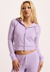 Helle lila Zip-Hoodie mit cropped Design, Fronttasche und verstellbarem Kapuzenzug. Weicher Stoff mit dezentem Logo-Detail auf der Brust.