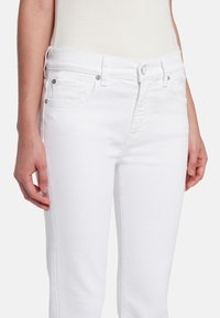 Witte denim jeans met een aansluitend ontwerp, voorzien van voorzakken, een knoopsluiting en subtiele stiksel details langs de naden.