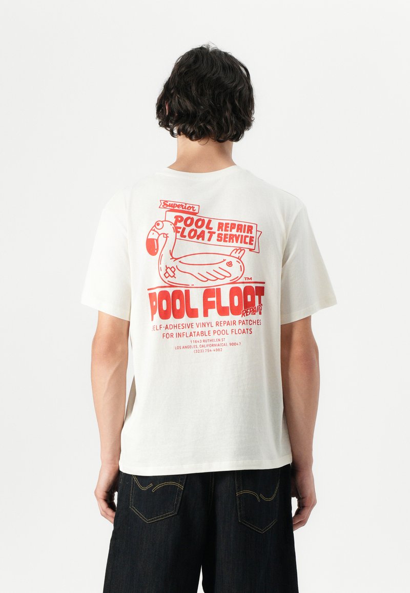 White cotton t-shirt featuring a red graphic design on the back, highlighting a pool float with text detailing a repair service.