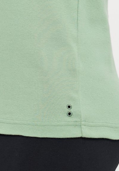 Chemise verte menthe à manches courtes avec une texture lisse. Possède un col rond et deux petits détails en œillet près de l'ourlet.