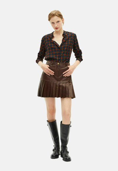 Bruine leren geplooide rok met een aansluitende taille, gecombineerd met een zwart shirt met een kleurrijk bloemenpatroon. Zwarte kniehoge laarzen.