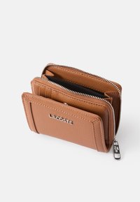 Lærbrun lommebok med teksturert overflate, glidelås og sølvfarget hardware. Har flere kortlommer og Lacoste-logoen på forsiden.