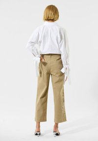 Weiße, kurz geschnittene Bluse mit gebundenen Ärmel, kombiniert mit khakifarbenen, weit geschnittenen Hosen mit floralem Stickmuster an der Seite. Einfaches Design und Farben.