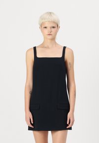 Robe sans manches noire avec un décolleté carré, dot�ée de deux poches avant. Fabriquée en tissu lisse, elle présente un design minimaliste et une coupe droite.