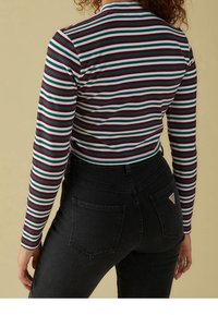 Pitkähiha, istuva paita, jossa on monivärisiä vaakaraitoja punaisessa, vihreässä ja valkoisessa. Yhdistetty korkeavyötäröisten mustien farkkujen kanssa, joissa on taskut.