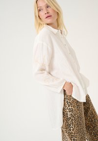 White button-up shirt with long sleeves and delicate gold embroidery. Paired with patterned beige and brown leopard print pants.