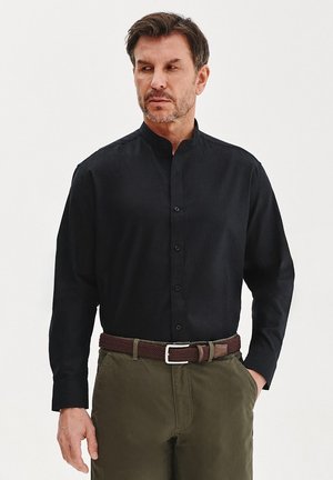 Czarna, długosleeve'owa koszula zapinana na guziki z kołnierzykiem w stylu band, w zestawie z oliwkowymi spodniami i plecionym brązowym paskiem. Gładka tekstura, dopasowany krój.