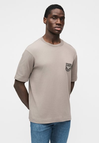 Light gray short-sleeve t-shirt with a round neckline, chest pocket, and embroidered logo detail. Fabric is smooth and slightly textured.