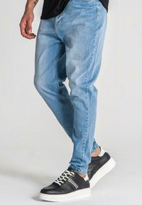 Ljusblå denimjeans med en tapered fit, kombinerat med svarta sneakers med vit plattform och färgade snören, i en avslappnad stil.