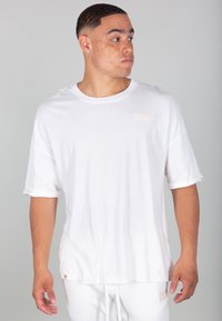 T-shirt bianca oversize realizzata in tessuto morbido, con scollo rotondo, maniche corte arrotolate e una piccola toppa con logo texturizzato sul petto.
