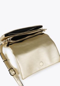 Zlatá kabelka s lesklým povrchem, která má dva zipy a černý interiér. Je k ní připevněn tenký, nastavitelný popruh.