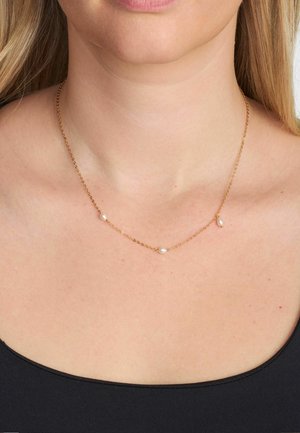 Auksinė grandinėlė su trimis mažais baltais perlų karoliukais tolygiai išdėstytais. Paprastas, subtilus dizainas, tinkantis nešioti sluoksniuotai arba vieną atskirai.