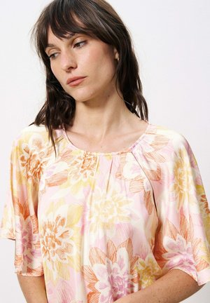 Haut floral léger avec une base rose et des motifs de fleurs jaunes et oranges, un col rond et des manches courtes et relaxed.