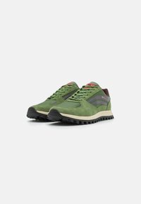 Ein Paar grüne Low-Top-Sneaker mit schwarzen Sohlen, beigen Zwischensohlen, roten Akzenten und seitlichen Streifen auf weißem Hintergrund.