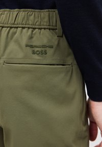 Παντελόνι ελιάς με ελαστική μέση, πίσω τσέπη και ανάγλυφο λογότυπο «Porsche BOSS» στην περιοχή της μέσης.
