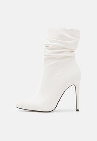 Bottine blanche en matériau synthétique lisse, avec un design décontracté, un bout pointu et un talon aiguille haut.