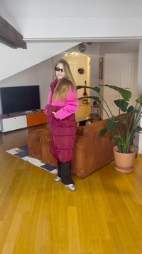 Lang vattert kåpe i mørk burgunder med livlige rosa aksenter; har høy krage og lommer. Sølvsko og slanke, mørke bukser fullfører antrekket.