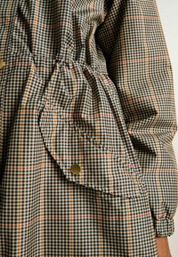 Pārbaudīta krekla ar zilu, beigu un sarkanu rakstu, ar savilkuma detaļām un pogu kabatu. Izgatavots no viegla auduma.