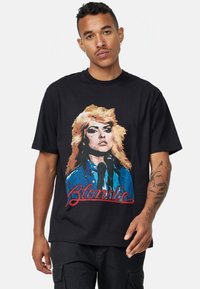 Černé bavlněné tričko s vintage grafikou ženy se světlými vlasy a mikrofonem, na které je překryto textem "Blondie" v červené barvě.