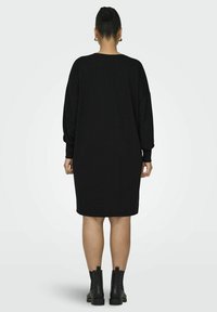 Abito maglione nero oversize con maniche lunghe, polsini a coste e scollo rotondo. Indossato con stivaletti neri alla caviglia con dettagli borchiati.