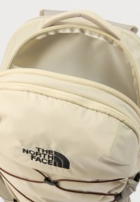 Μπεζ σακίδιο πλάτης The North Face με υφασμάτινη υφή, κλείσιμο με φερμουάρ, μπροστινή θήκη και μαύρο λογότυπο. Ρυθμιζόμενο κορδόνι τύπου bungee.