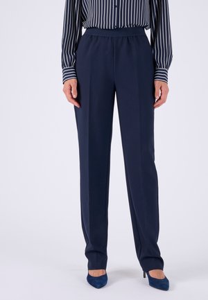 Donna che indossa pantaloni dritti blu navy, tacchi a punta blu navy e una camicia a righe verticali blu navy e bianche.