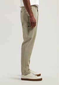 Světle zelené cargo kalhoty se bočními kapsami a rovný střih, doplněné bílými teniskami. Tkanina vypadá hladce s jemným leskem.