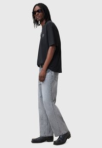 Camiseta negra de gran tamaño con gráfico de corazón, pantalones de mezclilla anchos en gris y botas de cuero negras, con una textura suave y un ajuste relajado.