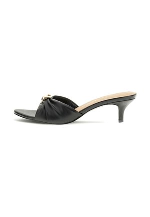 Mule en cuir noir à bout ouvert, talon kitten, bride froncée avec détail chaîne dorée sur fond blanc.