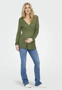 Groene, geribbelde wikkel top met lange mouwen en een diepe V-hals, gecombineerd met strakke blauwe jeans en witte sneakers. Glad, rekbaar materiaal.