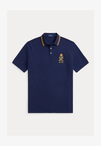 Marineblå polo-skjorte med krage med gule og røde striper, brodert logo med en krone og detalj med 'EST. 1967'. Mykt bomullsmateriale.