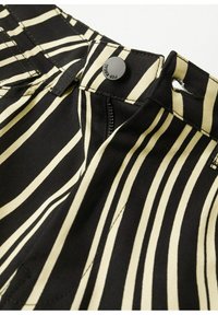 Černobílý pruhovaný materiál s detailním záběrem na zapnutý pás a zip, který ukazuje hladkou strukturu a precizní šití.