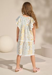 Blumengemustertes Stufenkleid in Pastellgelb- und Blautönen, mit Rüschenärmeln, Spitzensaum und Knopfverschluss auf der Rückseite.
