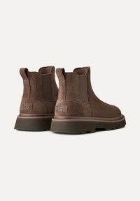 Stivaletti in suede marrone con pannelli laterali elasticizzati e una suola in gomma spessa. Presenta un piccolo etichetta con logo sul tallone e una finitura testurizzata.