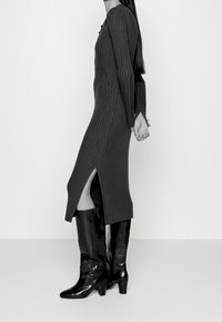 Lång, ribbad klänning i mörkgrått med en slits på sidan, ihop med knähöga svarta lackskinnstövlar med klumpig klack.