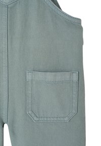 Helle grüne Latzhose aus strukturiertem Denim, mit verstellbaren Trägern und einer runden Taschen auf der Vorderseite.