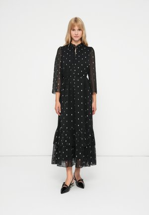 Vestido maxi negro con mangas de tres cuartos, patrón de lunares, dobladillo con volantes y detalle de cinturilla con lazo, hecho de tela ligera y transparente.