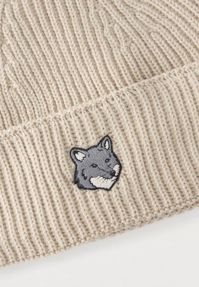 Tela de punto beige acanalada con un pequeño parche bordado de cara de zorro gris cosido en la parte inferior central.
