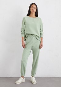 Lichtgroene sweatshirt met geribde manchet en ronde halslijn, gecombineerd met bijpassende taps toelopende sweatpants met een elastische tailleband. Casual schoeisel.
