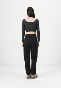 Pantaloni cargo negri cu buzunare laterale, asortați cu un crop top gri, ajustat și cu dungi. Topul are un decolteu larg și mâneci lungi.