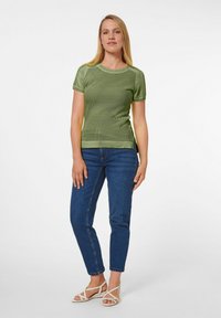 Grünes geripptes Kurzarmoberteil mit Rundhalsausschnitt, kombiniert mit blauen Jeans und hellen Sandalen mit Riemchen. Strukturierter Stoff, enganliegendes Design.